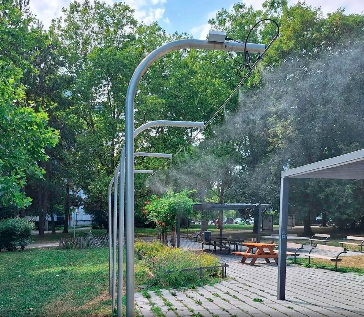 High-pressure misting showers on metal arches in a Vienna park, trees and picnic tables behind